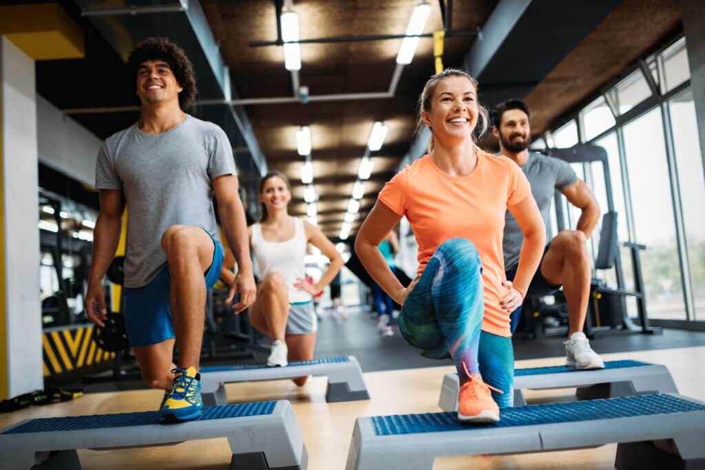 Quatre personnes souriantes font du step en groupe dans une salle de sport moderne. Deux hommes et deux femmes, motivés pour l'entraînement physique.